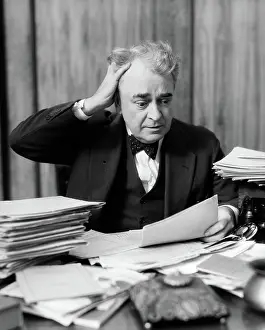 Melodramatic: Elderly businessman sitting at desk among stacks