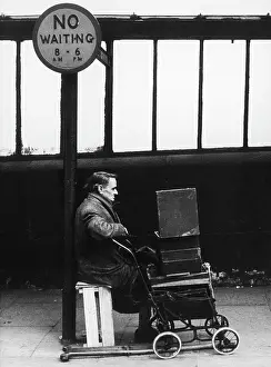 Signage: Elderly disabled man sits alone beneath a No Waiting sign
