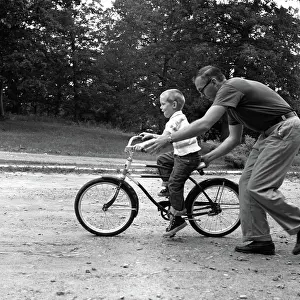 Pedaling: Father giving son on bike a push teaching him