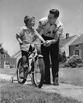 Camerique: Father helping son learn to ride a bike with training wheels