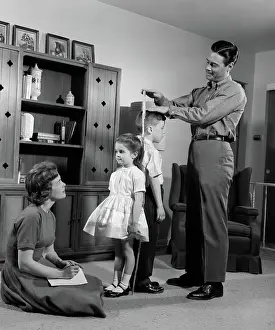 Taller: Father measuring daughter & son back-to-back