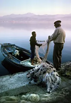 Timeless: Two fishermen sort their nets on stone quayside - Fetheye