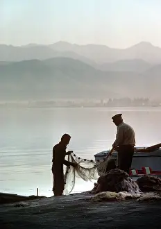 Timeless: Two fishermen sort their nets on stone quayside - Fetheye