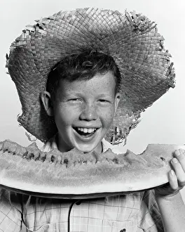 Wedges: Freckle-faced boy wearing straw hat eating large