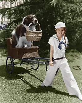 Wholesome: Girl in sailor suit pulling dog in basket