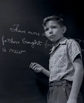 Schoolrooms: Grade school boy at chalkboard writing out gettysburg