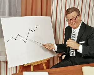 Profits: Happy Businessman Looking at Camera Pointing to Graph