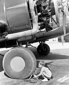 Safeguard: Little boy crouching by the wheel of a plane