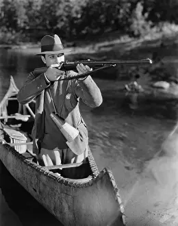 Fedora: Man aiming gun from canoe