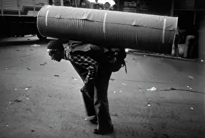 Courier: A man carrying a huge roll of heavy material on his back