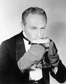 Uncommon: Man drinking a big glass of cold beer with mittens