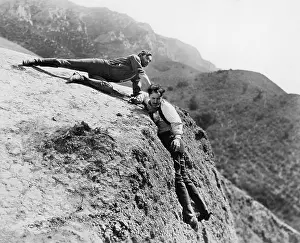 Cooperate: Man helping another man from falling down a cliff