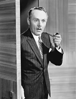 Displeasure: Man holding a pipe and standing at a doorway looking