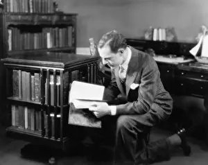 Browsing: Man kneeling in his home library browsing a book