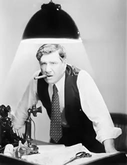 Glows: Man leaning over a desk with a ceiling light shining on him
