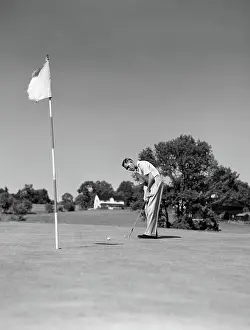 Putter: Man playing golf putting golf ball on green to