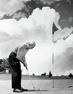 Putter: Man playing golf putting golf ball on green to