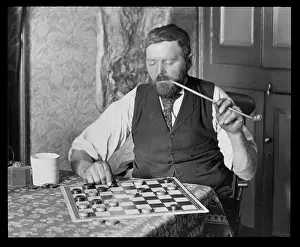 Cupboard: Man puzzling over a game of draughts