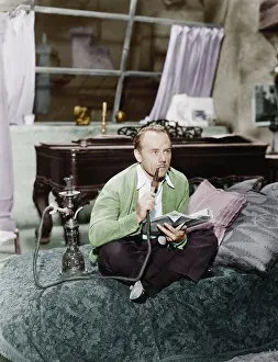Close Crop: Man sitting on a bed smoking his water pipe