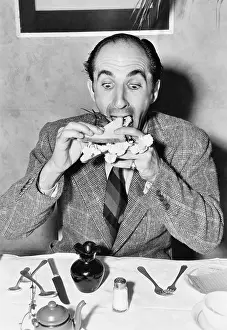 Shaker: Man sitting at a dining table and trying to eat a sandwich