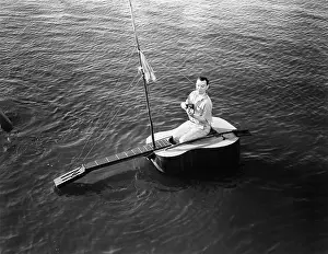 Everett Collection (old Visuals): Man sitting on a guitar sailboat