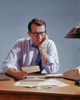 Unease: Man Sitting at Table with Pile of Bills Paperwork and W