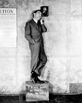 Midadult: Man standing on a box to reach the telephone