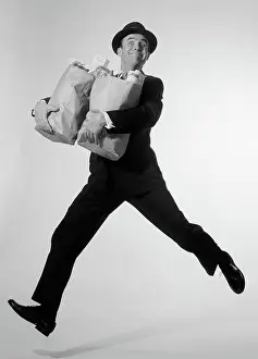 Aerobic: Man in suit & fedora leaping forward with grocery