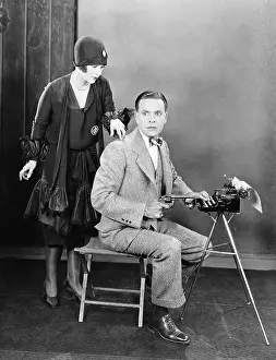 Startling: Man at a typewriter holding a gun and a woman tapping