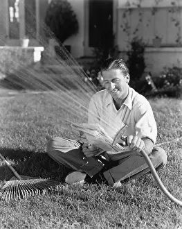 Multitask: Man watering the grass and reading