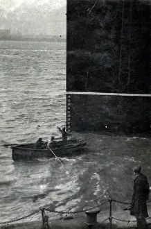 Prow: Three men in a rowing boat dwarfed next to prow of a steamer
