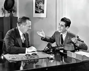 Networking: Two Men Seated at Desk Younger Man Talking Gesturing