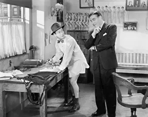 Employ: Two men standing in an office, one ironing his pants