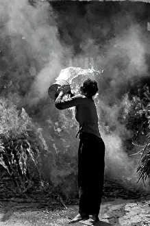 Refugee: An old woman tries to extinguish burning thatch