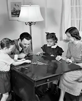 Tabletop: Parents playing pick up sticks game with young