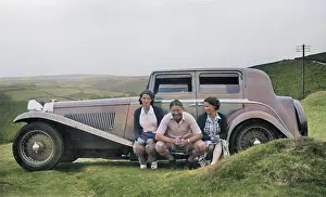 Three people sitting on running board of car
