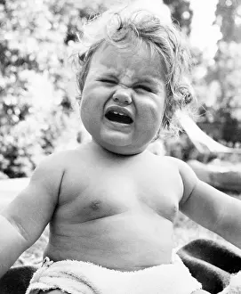 Frowning: Plump baby crying in a garden