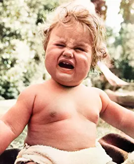 Frowning: Plump baby crying in a garden