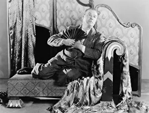 Unkempt: Portrait of a man sitting on a couch holding a fan