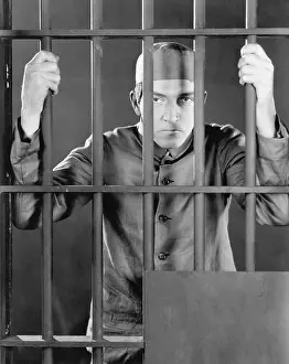 Clasping: Prisoner behind bars looking angry and sad