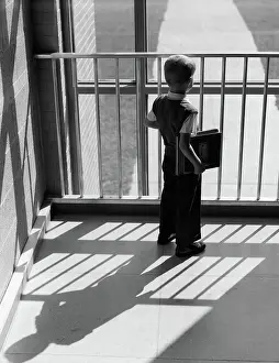 Outcast: Schoolboy with books under arm looking out window