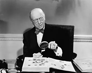 Examinations: Senior man examining a postage stamp with a magnifying