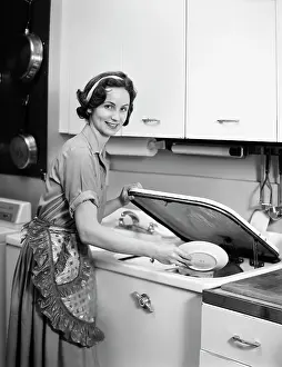 Dishwasher: Smiling Housewife Loading Dishwasher Looking at Camera