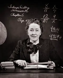 Prissy: Smiling Middle Aged School Teacher at Desk Beside Globe