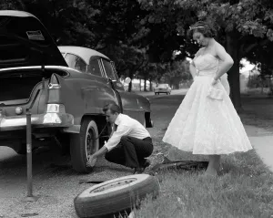 Whitewall: Teenage boy crouching down changing flat tire