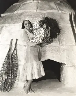 1910s 1940s: Woman carrying gift boxes outside igloo