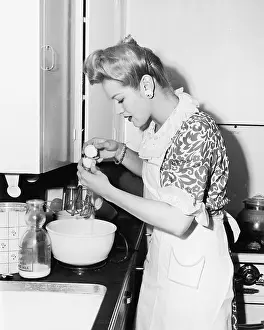 Cracking: Woman in the kitchen cracking an egg