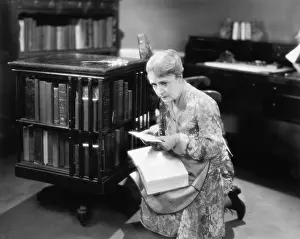 Insecure: Woman kneeling with a book in her library finding a letter