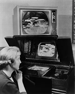 Horizontally: Woman looking at two television sets. One, ?