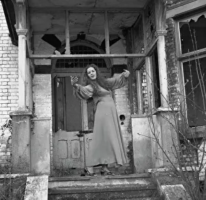 Panes: Woman posing in front of a derelict house